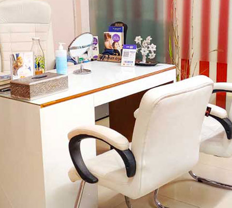 Dr. Poonam Arya's white colored office desk and chairs. Items on desk incliude a mirror, tissue box and hand sanitiser