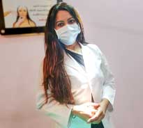 Dr. Poonam Arya standing in her clinic, wearing white coat and operating equipment