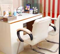 Dr. Poonam Arya's white colored office desk and chairs. Items on desk incliude a mirror, tissue box and hand sanitiser